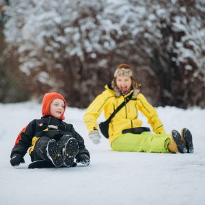 Mother and son enjoying winter activity, actively sledding down a snowy slope, bonding and having fun outdoors