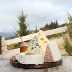 Different types of delicious cheeses on wooden table against mountain landscape